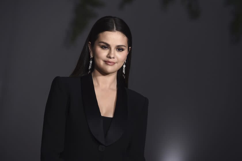 A woman with long black hair posing in a black suit