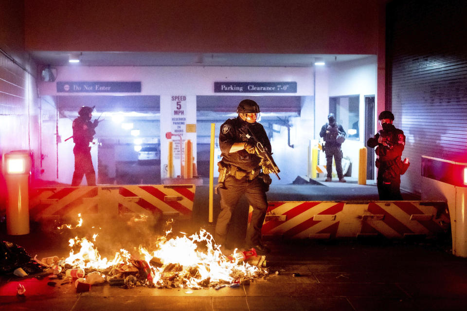 A Department of Homeland Security officer emerges from the Mark O. Hatfield United States Courthouse after demonstrators lit a fire on Sunday, Aug. 2, 2020, in Portland, Ore. Following an agreement between Democratic Gov. Kate Brown and the Trump administration to reduce federal officers in the city, nightly protests remained largely peaceful without major confrontations between protesters and officers. (AP Photo/Noah Berger)