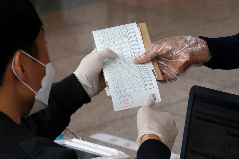 A poll worker hands out a voting pass at a polling station in Seoul