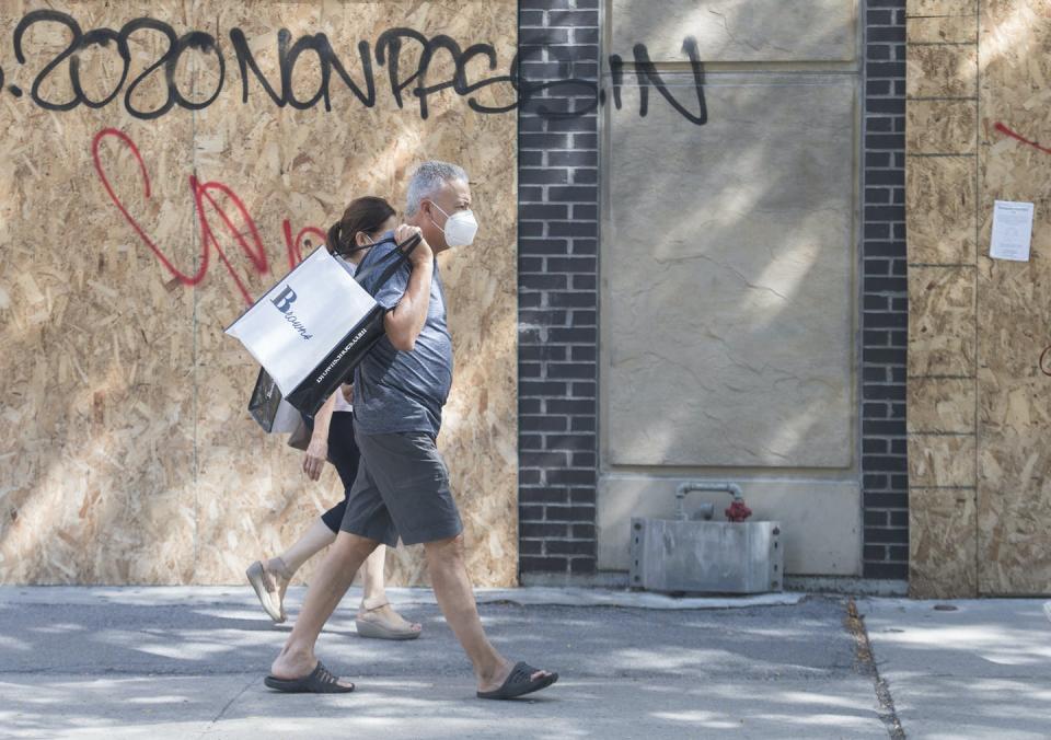 People wearing face masks walk past a boarded-up storefront.