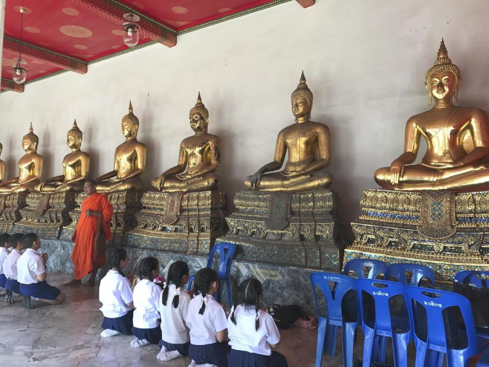 In this Dec. 9, 2016 photo, monks teach schoolchildren religious incantations at Wat Pho, or the Temple of the Reclining Buddha, in Bangkok. Between lessons, the kids waved and called greetings to tourists. (AP Photo/Courtney Bonnell)