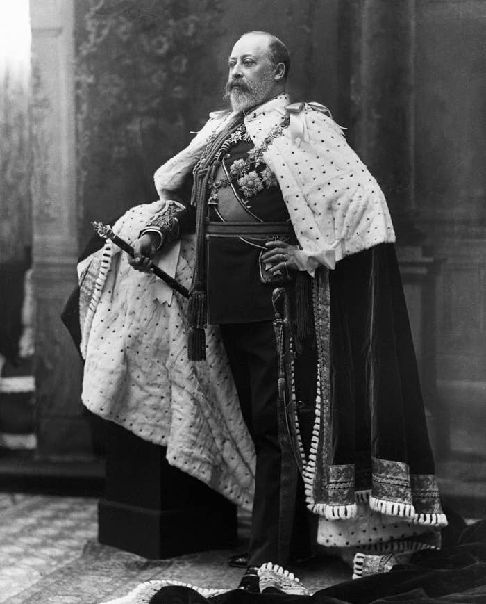 King Edward VII stands in a formal pose, wearing regal attire including a ceremonial robe, sash, and holding a scepter