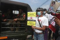 Protester holds a sign that reads 'We Want Justice' next to soldiers deployed outside the Central Bank of Myanmar building in Yangon, Myanmar on Monday, Feb. 15, 2021. Myanmar's military leaders have extended their detention of Aung San Suu Kyi, whose remand was set to expire Monday and whose freedom is a key demand of the crowds of people continuing to protest this month's military coup. (AP Photo)