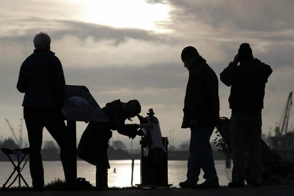 Viewers look on during a brief break in the clouds to see a transit of the planet Mercury as it crosses the face of the sun Monday, Nov. 11, 2019, as seen from Seattle. Mercury and Venus are the only planets that can appear to pass in front of, or transit, the sun as seen from Earth. (AP Photo/Elaine Thompson)