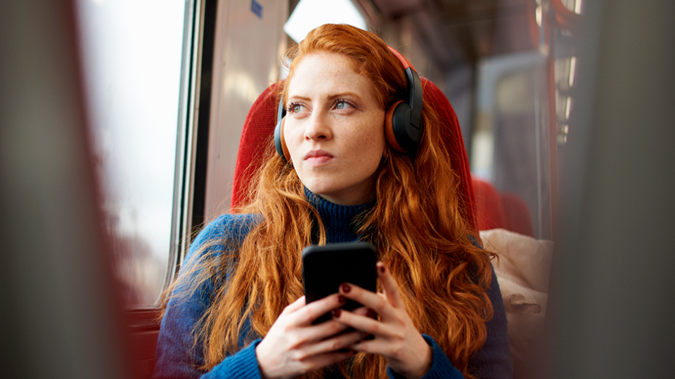 Image of young woman listening to podcast on train, looking intense true crime representation