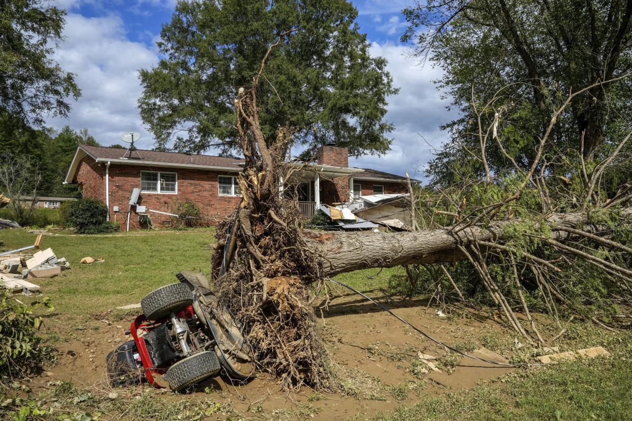 An overturned tractor lies next to an uprooted tree on the White family' property in the aftermath of Hurricane Helene, Tuesday, Oct. 1, 2024 in Morganton, N.C. The adjacent Catawba River flooded due to torrential rains destroying seven of the family's nine homes on the property. (AP Photo/Kathy Kmonicek)