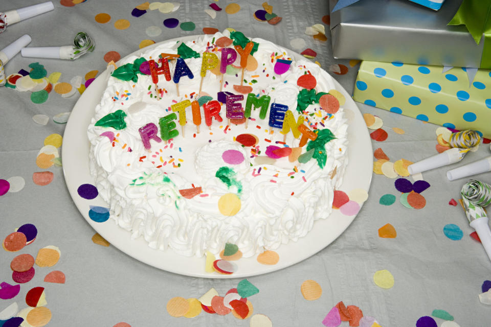 A retirement cake with "Happy Retirement" lettering surrounded by confetti and party blowers on a table