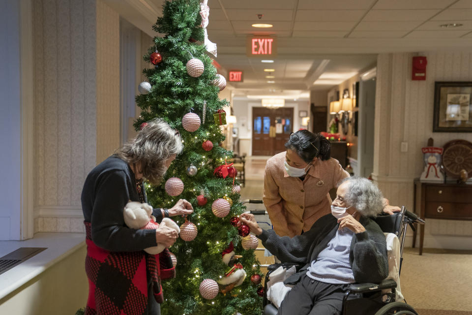 Tina Sandri, CEO of Forest Hills of DC senior living facility, center, greets residents Cherie Neville, left, and Catherine Doleman on Thursday, Dec. 8, 2022, in Washington. As nursing home leaders redouble efforts to get staff and residents boosted with the new vaccine version, now recommended for those 6 months and older, they face complacency, misinformation and COVID-19 fatigue. (AP Photo/Nathan Howard)