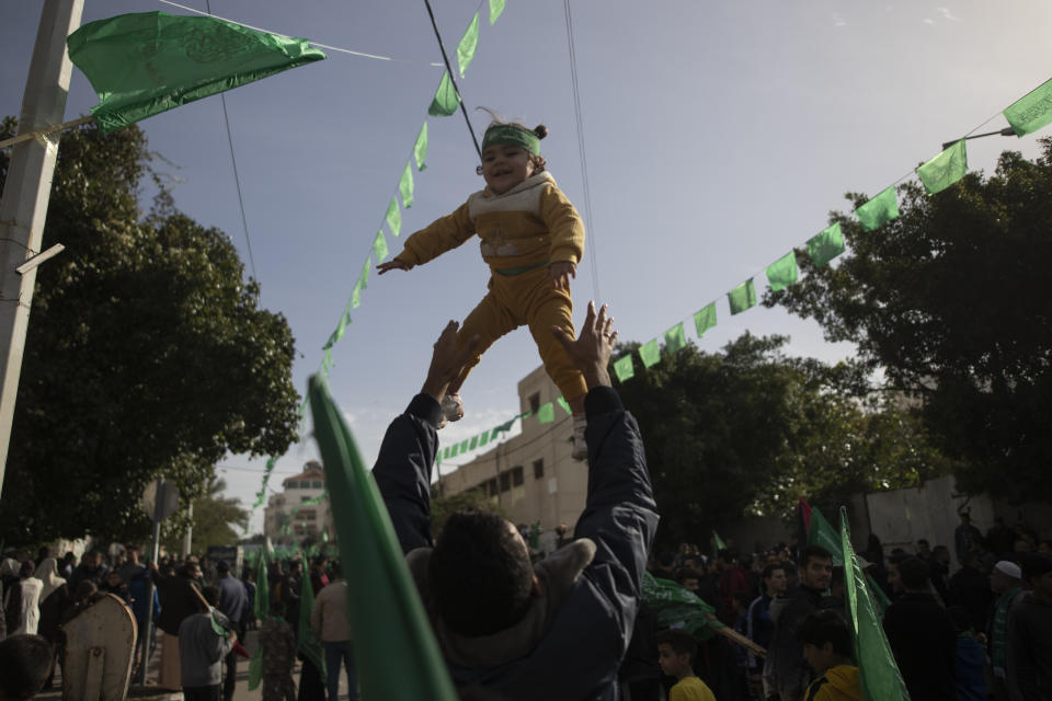 A Palestinian man plays tosses his child during a rally marking the 34th anniversary of Hamas movement's founding, in Gaza City, Friday, Dec. 10, 2021. Gaza’s Hamas rulers collect millions of dollars a month in taxes and customs at a crossing on the Egyptian border – providing a valuable source of income that helps it sustain a government and powerful armed wing. After surviving four wars and a nearly 15-year blockade, Hamas has become more resilient and Israel has been forced to accept that its sworn enemy is here to stay. (AP Photo/ Khalil Hamra)