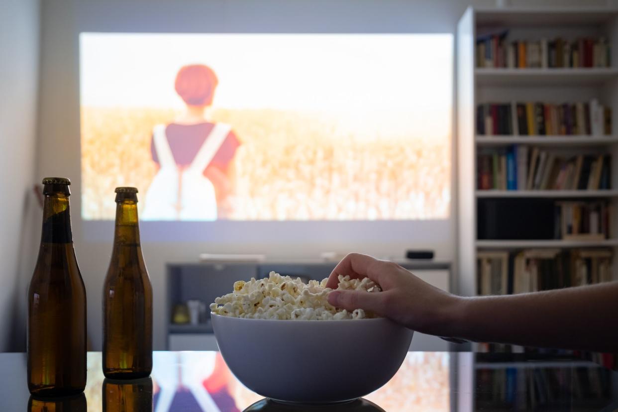 Dim living room with a cinematic picture projected on the wall, human hand grabbing popcorn