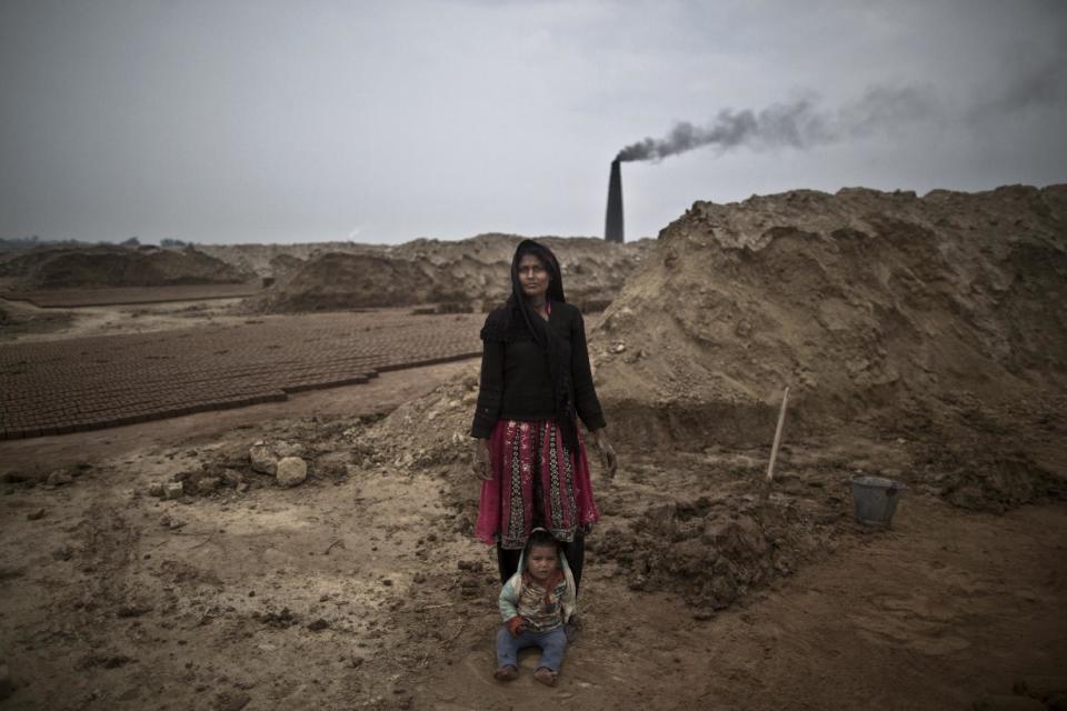 In this Monday, March 3, 2014, photo, Rubina Rafaqat, 22, a Pakistani brick factory worker, poses for a picture with her child at the site of her work in Mandra, near Rawalpindi, Pakistan. Rubina and her husband are in debt to their employer the amount of 200,000 rupees (approximately $2000). (AP Photo/Muhammed Muheisen)