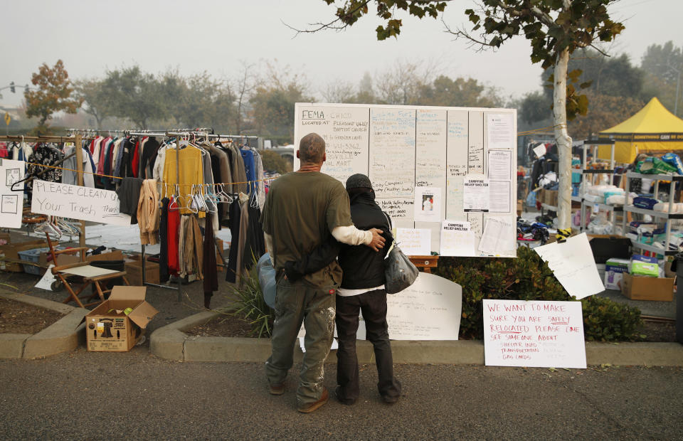 Tera Hickerson, derecha, y Columbus Holt se abrazan mientras buscan información en una pizarra afuera de una tienda Walmart para gente desplazada por el incendio forestal el viernes 16 de noviembre de 2018 en Chico, California. (AP Foto/John Locher)