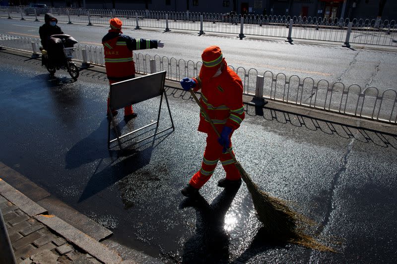 A workers wears a face mask as he sweeps the street after it was sprayed with disinfectant in Beijing as the country is hit by an outbreak of the novel coronavirus