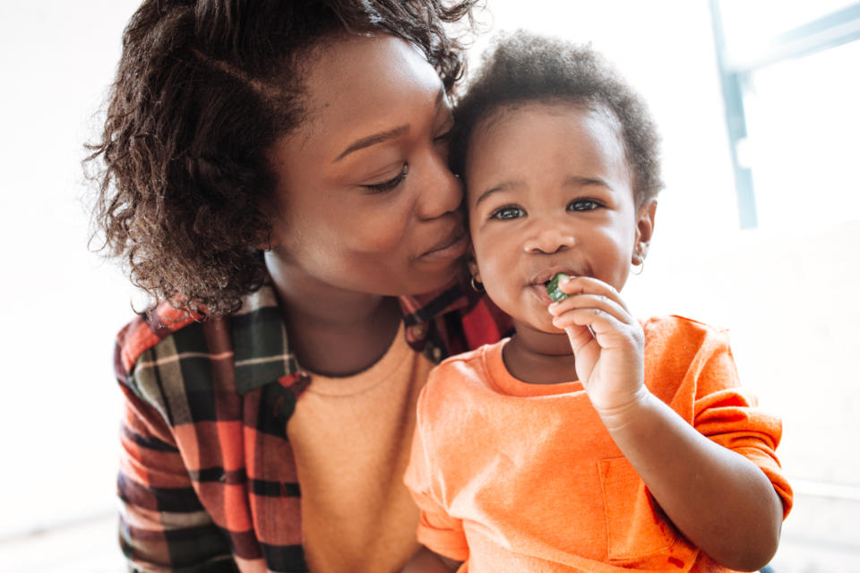 A parent gently kisses their child on the cheek while the child eats a snack