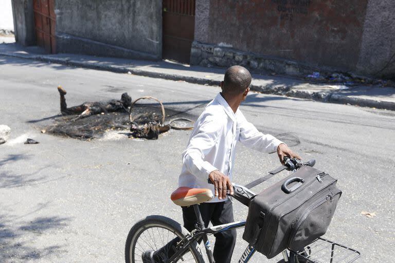 Un hombre empuja su bicicleta junto al cuerpo de una persona que fue asesinada e incendiada en Puerto Príncipe, Haití, el martes 5 de marzo de 2024.
