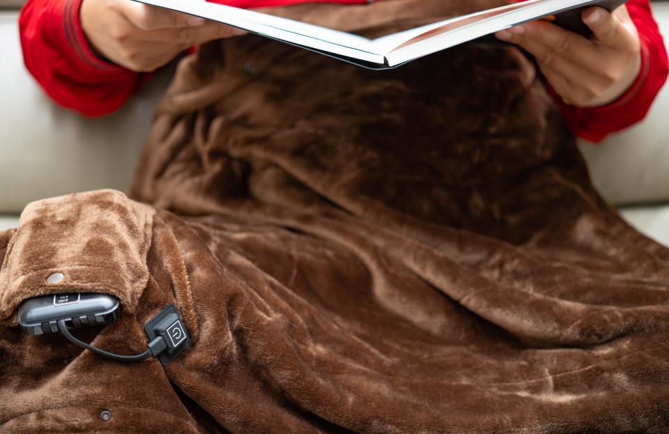 Man with an electric blanket and reading a book on a sofa