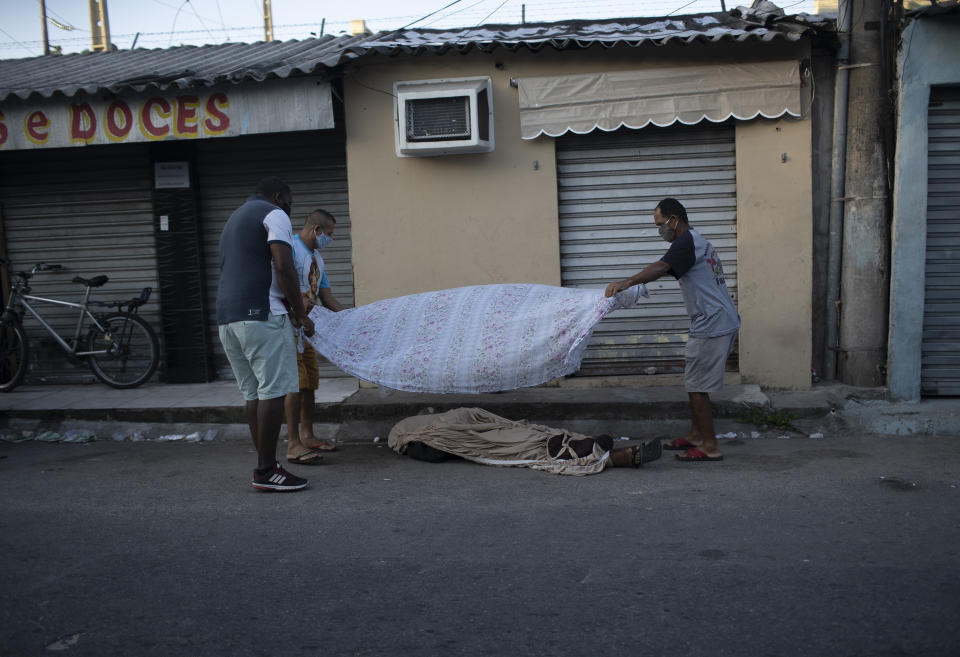 Neighbors cover the the body of Luiz Carlos Da Rocha, 36, with a sheet, as he lies on a street where he dropped dead at the Alemao Complex slum of Rio de Janeiro, Brazil, Tuesday, April 28, 2020. After more than 12 hours on the street the body of Da Rocha, who the family said suffered from epilepsy, had not been picked up by authorities. Military police said that due the new coronavirus pandemic, they only can remove corpses in cases of violent death. (AP Photo/Silvia Izquierdo)