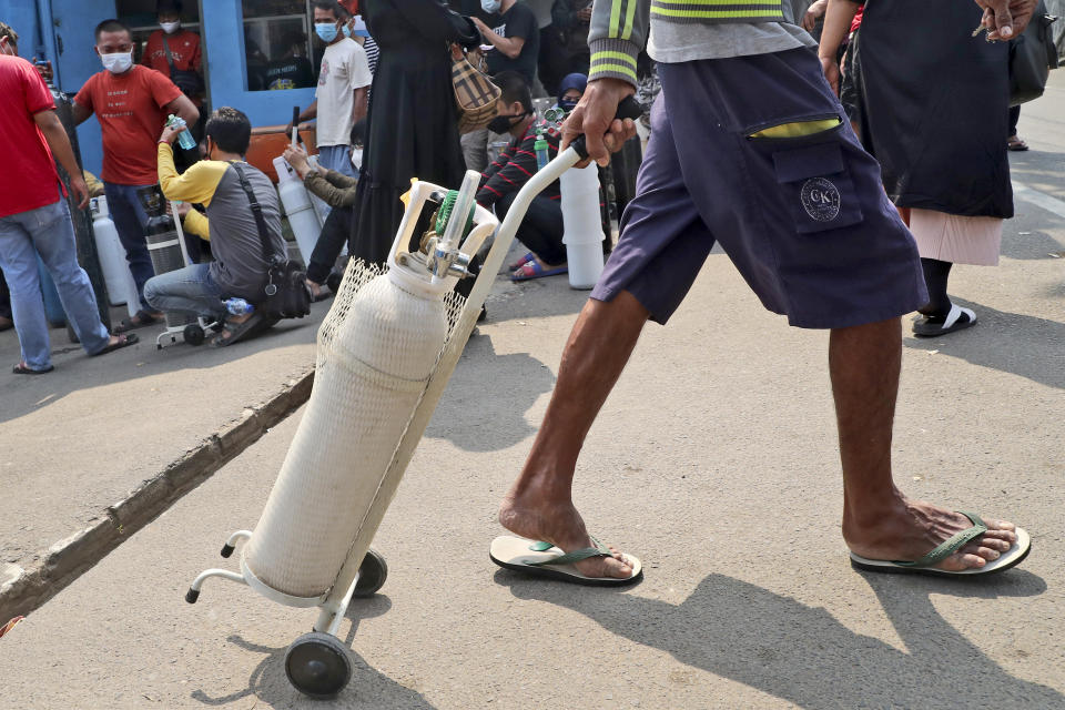 A man leaves with his full oxygen canister as others wait to refill their tanks at a recharging station in Jakarta, Indonesia, Friday, July 9, 2021. Just two months ago, Indonesia was coming to a gasping India's aid with thousands tanks of oxygen. Now, the Southeast Asia country is running out of oxygen as it endures a devastating wave of coronavirus cases and the government is seeking emergency supplies from other countries, including Singapore and China. (AP Photo/Tatan Syuflana)