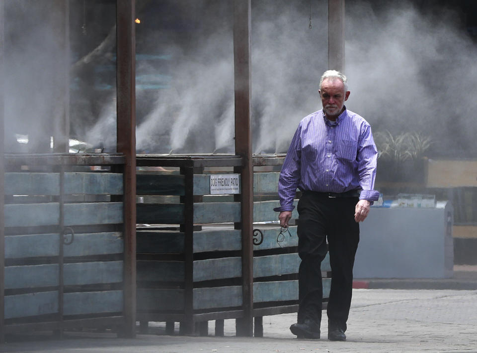 A man walks through cooling misters, Tuesday, July 24, 2018 in Tempe, Ariz. Much of Arizona and parts of California, Arizona and Utah are under an excessive heat watch during a week that forecasters say could prove to be the hottest of the year. (AP Photo/Matt York)