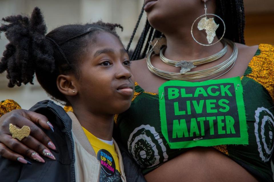 Una mujer con el mensaje "Las vidas negras importan" abraza a una niña en Londres durante una protesta el 20 de marzo de 2022.