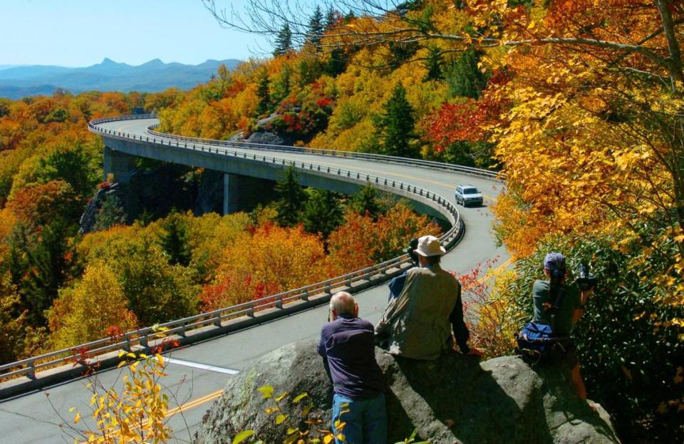 Photographers crowd a rock above the Linn Cove Viaduct to shoot the fall colors along the Blue Ridge Parkway at Grandfather Mountain.