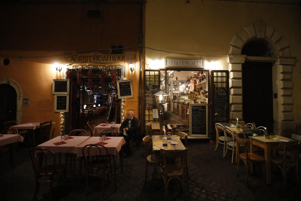 A man sits outside an empty restaurant in Rome's Trastevere neighborhood, Friday, Oct. 23, 2020. In much of Europe, city squares and streets, be they wide, elegant boulevards like in Paris or cobblestoned alleys in Rome, serve as animated evening extensions of drawing rooms and living rooms. As Coronavirus restrictions once again put limitations on how we live and socialize, AP photographers across Europe delivered a snapshot of how Friday evening, the gateway to the weekend, looks and feels. (AP Photo/Alessandra Tarantino)