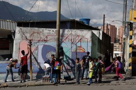 Children watch as artists paint a mural over a wall in Petare Slum, in Caracas