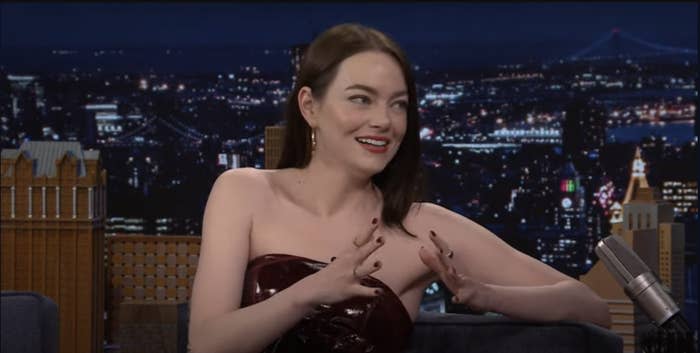 Emma Stone speaks animatedly on "The Tonight Show Starring Jimmy Fallon", wearing a strapless outfit, with a cityscape backdrop