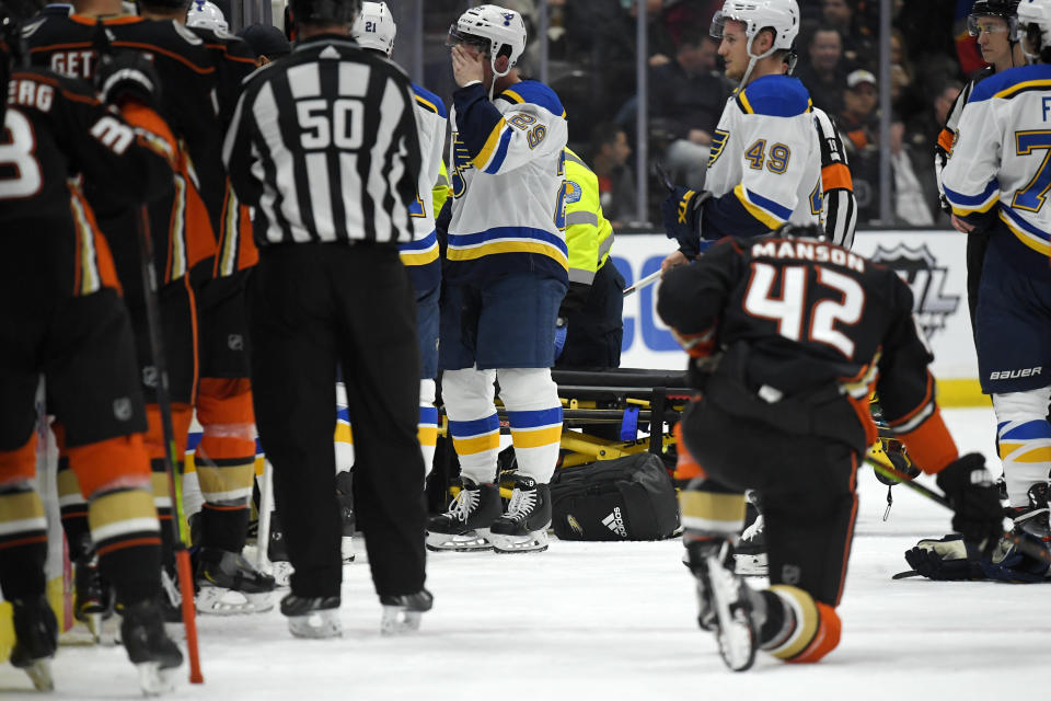 St. Louis Blues defenseman Vince Dunn, left, of center wipes his faces as Anaheim Ducks defenseman Josh Manson kneels on the ice while blues defenseman Jay Bouwmeester, who suffered a medical emergency, is worked on by medical personnel during the first period of an NHL hockey game Tuesday, Feb. 11, 2020, in Anaheim, Calif. (AP Photo/Mark J. Terrill)