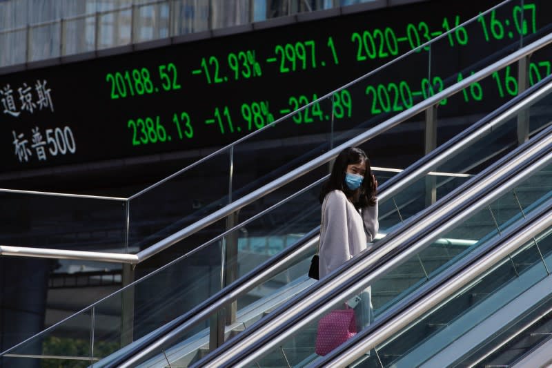 Pedestrian wearing a face mask rides an escalator near an overpass with an electronic board showing stock information in Shanghai