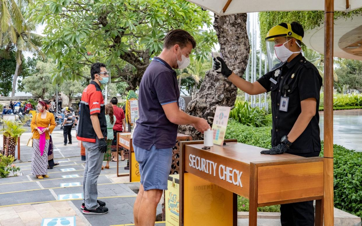 A security guard checks the temperature of a visitor at a reopened shopping mall in Bali, Indonesia - Shutterstock