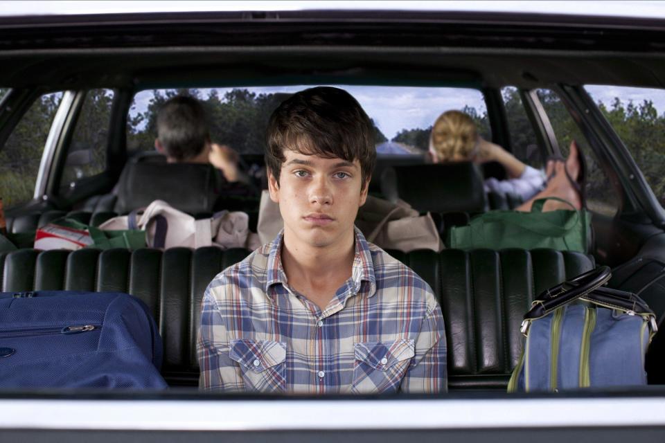 A young man stares despondently out of the rear window of his family's car