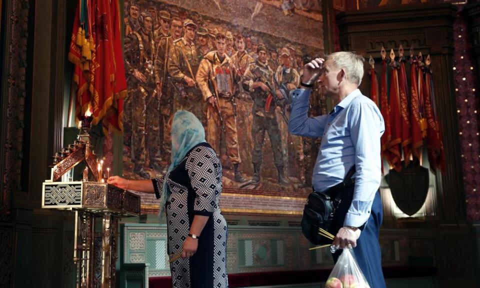 Russian Orthodox Christian light candles near a mosaic depicting more recent conflicts.