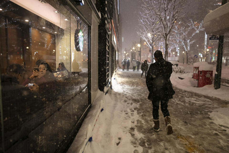 A man walks through a snow storm past a coffee shop Feb. 5, 2020, in Sapporo, Hokkaido, Japan. (AP Photo/Jae C. Hong)