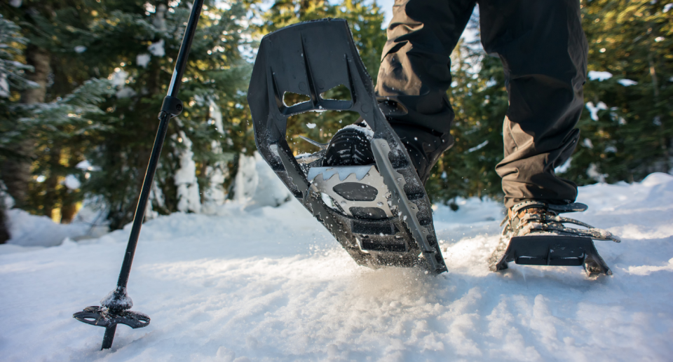 man walking in snoeshoes and trekking pole on snow in front of trees