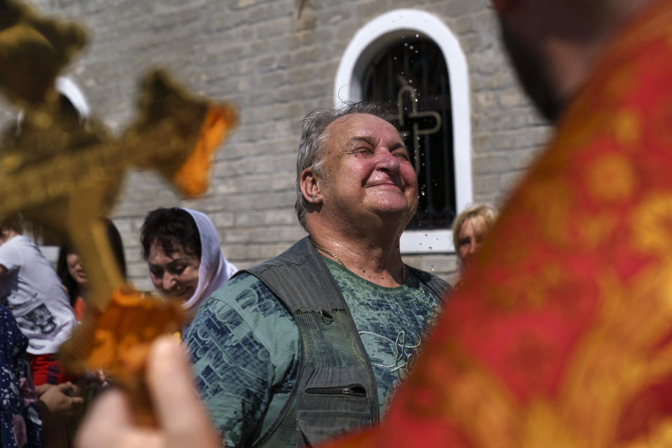 Archpriest Oleksandr Kondratyuk, right, blesses a congregant with holy water outside St. Michael's Ukrainian Orthodox Church of the Moscow Patriarchate for Savior of the Honey Feast Day in Pokrovsk, Donetsk region, eastern Ukraine, Sunday, Aug. 14, 2022. (AP Photo/David Goldman)