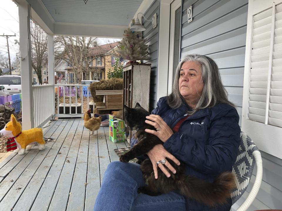 Kris Consaul, a Loudon County, Va., activist and former planning commissioner in Lovettsville, Va., discusses the lively politics and political divisions in her town, Dec. 18, 2021, as her chickens roam on her porch. Consaul says frictions over Donald Trump's presidency and the social shutdown during part of the pandemic "pretty much ripped a hole through the center of town." But spirits were lifted when neighbors gathered to paint her fence in the rainbow colors of the gay-pride flag. It's become an attraction for visitors and residents alike, though some on the right object. (AP Photo/Cal Woodward