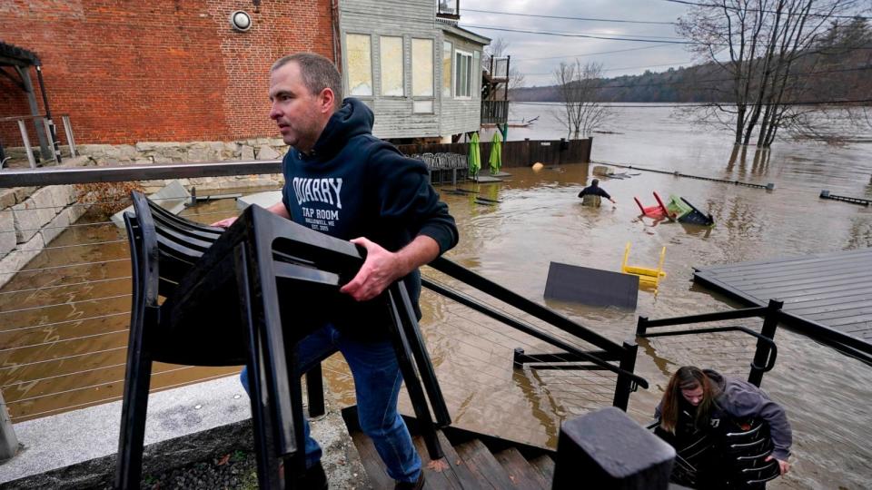 PHOTO: Joe Stanhope and Tori Grasse carry furniture from the flooded outdoor patio of the Quarry Tap Room, Dec. 19, 2023, in Hallowell, Maine.  (Robert F. Bukaty/AP)