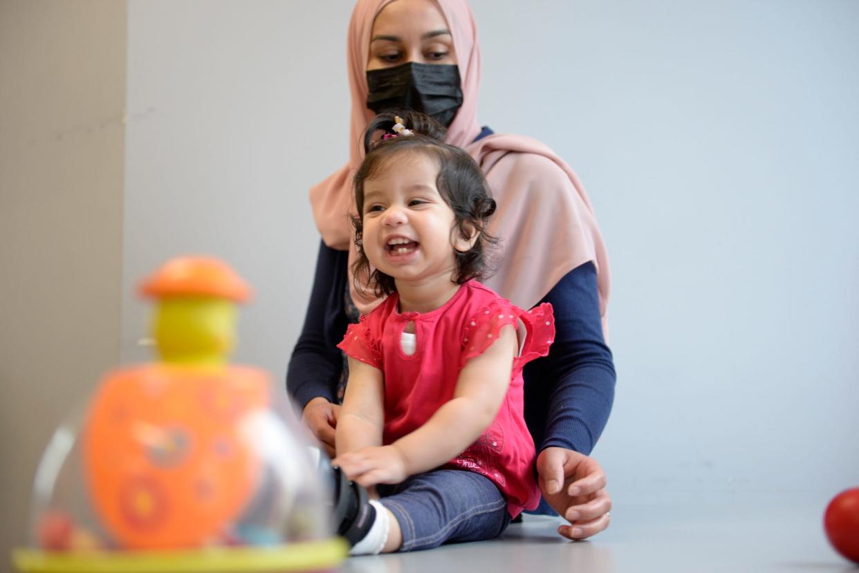 little girl smiling, playing on floor, with mom behind her