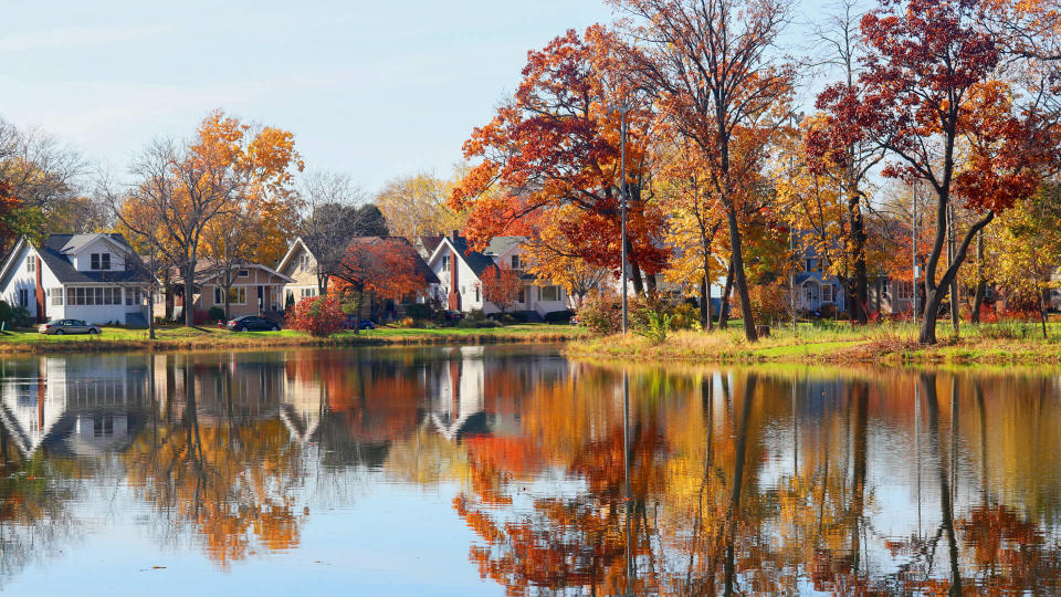 Fall view of private houses neighborhood with classic american middle class homes and colorful trees along a pond reflected in a water.