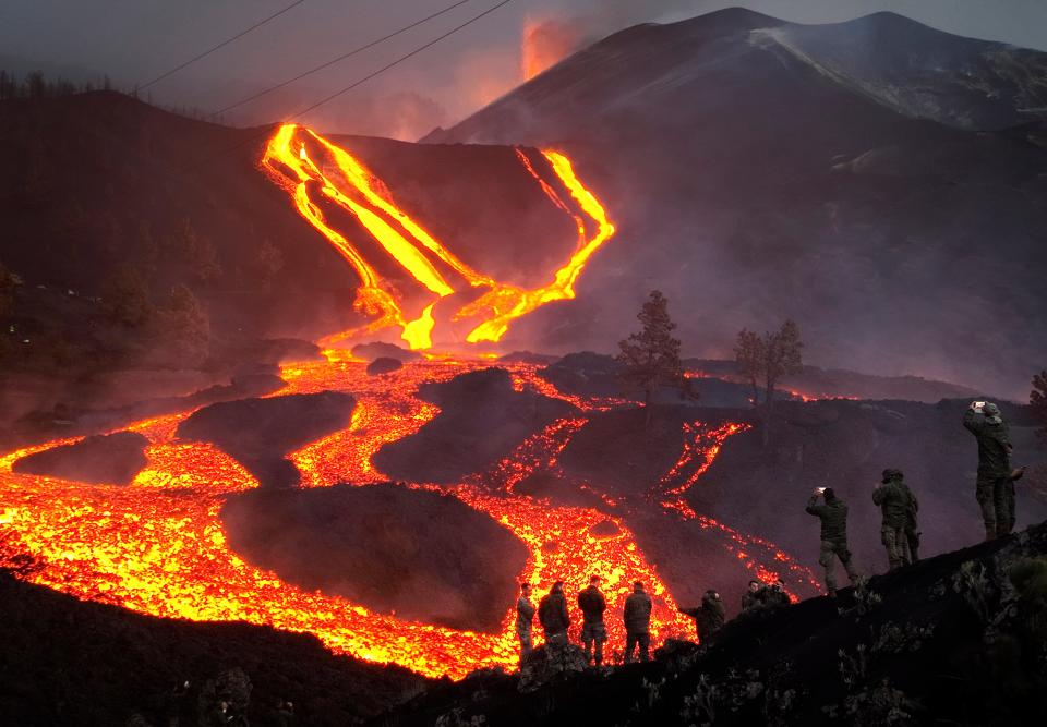 Spanish Army soldiers stand on a hill as lava flows as volcano continues to erupt on the Canary island of La Palma, Spain, Monday, Nov. 29, 2021. 