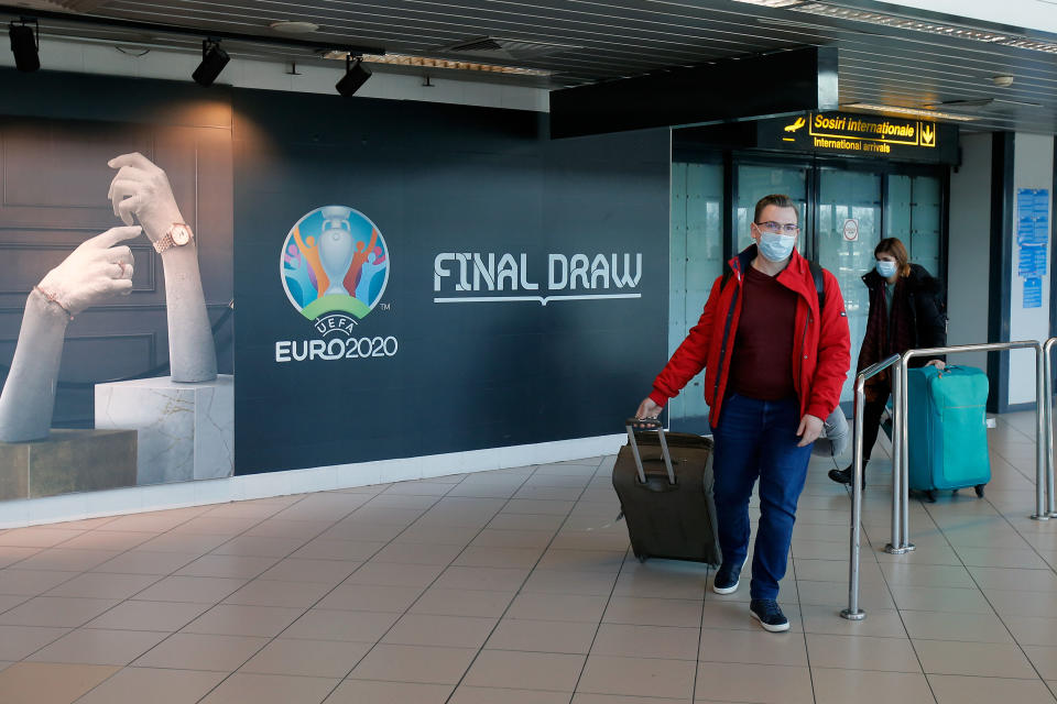 BUCHAREST, March 17, 2020 -- People wearing face masks pass a logo of the EURO 2020 European Football Championship displayed on a wall at Henri Coanda International Airport in Bucharest, Romania, March 17, 2020. The European football governing body UEFA has decided to postpone this summer's European Championship to 2021 due to the coronavirus outbreak.   Romanian President Klaus Iohannis announced that the country will enter an emergency state starting March 16, in an effort to ensure that the government uses all resources to fight the COVID-19 epidemic. (Photo by Cristian Cristel/Xinhua via Getty) (Xinhua/ via Getty Images)