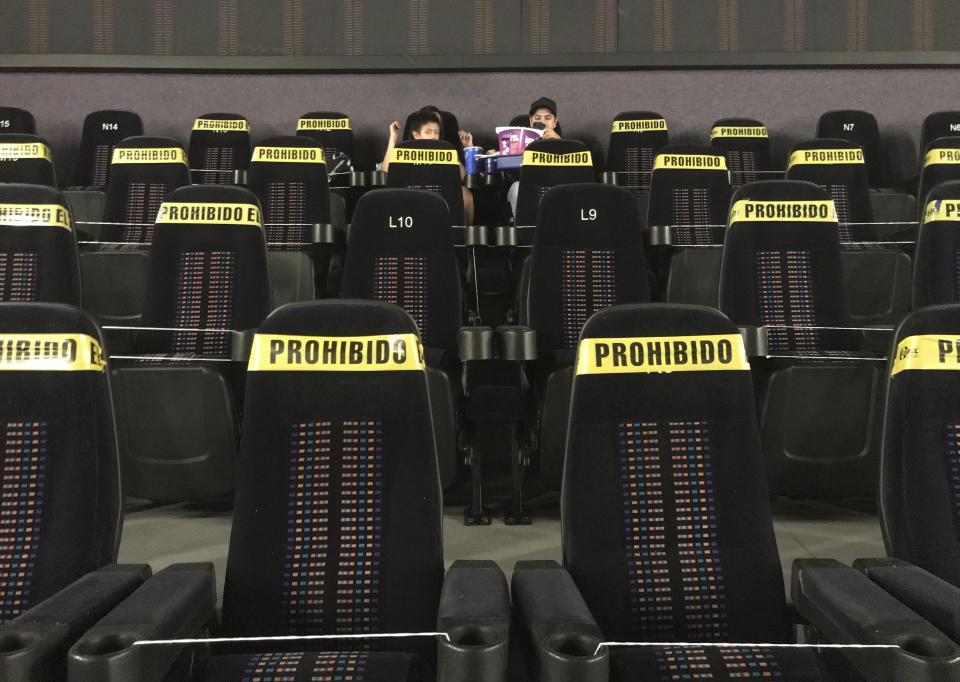 A couple of youths wait for the start of a movie, in an almost empty movie house with most of the seating blocked with yellow tape that reads in Spanish "Prohibited," to help curb the spread of the new coronavirus, in Mexico City, Tuesday, April 27, 2021. (AP Photo/Marco Ugarte)