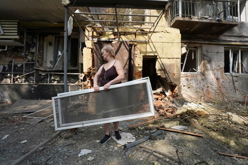 A woman holds window frames after a Russian attack that damaged some buildings in Kharkiv, Ukraine, Tuesday, Aug. 30, 2022. A surge in fighting on the southern front line and a Ukrainian claim of new attacks on Russian positions fed speculation Tuesday that a long-expected counteroffensive has started trying to turn the war's tide.