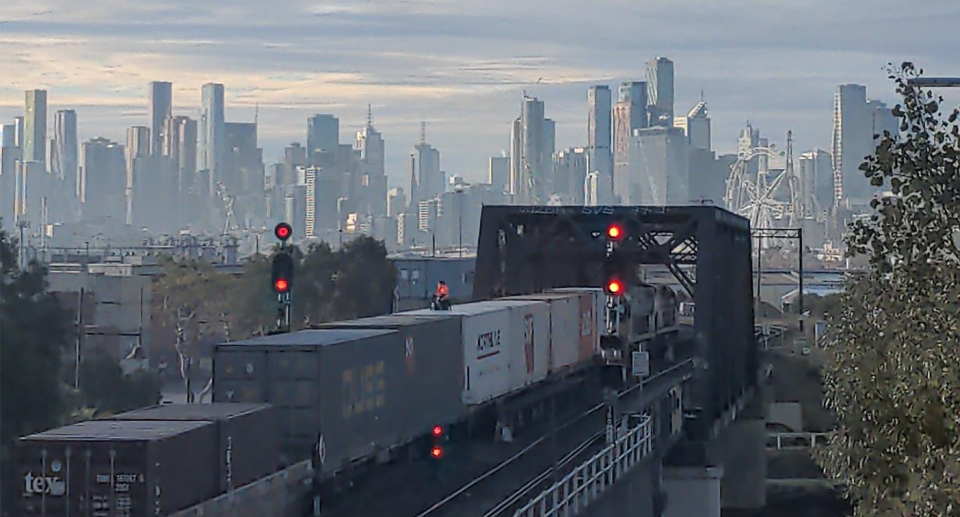A cargo train can be seen stopped on a bridge. The protester is a tiny speck on the carriage. The city of Melbourne can be seen in the background.