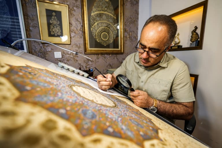 Mohammad Hossein Aghamiri, an artist who specialises in Persian miniatures, uses a magnifying glass as he works on one of his pieces depicting al-Fatiha, the first chapter of the Koran (ATTA KENARE)