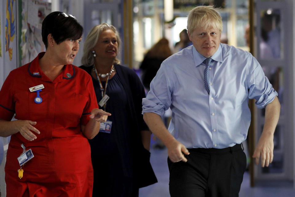 Britain's Prime Minister Boris Johnson is guided during a visit to the Royal Cornwall Hospital in Truro, south-west England, Monday Aug. 19, 2019. Johnson is under increasing pressure Monday to recall Parliament after leaked government documents warned of widespread problems if the U.K. leaves the European Union without a Brexit withdrawal agreement. (Peter Nicholls/Pool via AP)