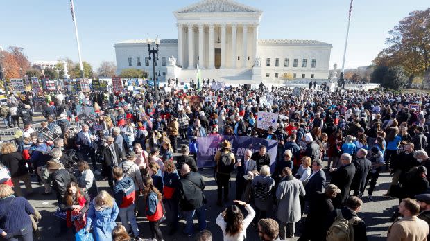 A large crowd of protesters gathers outside the US Supreme Court Building on a sunny day.