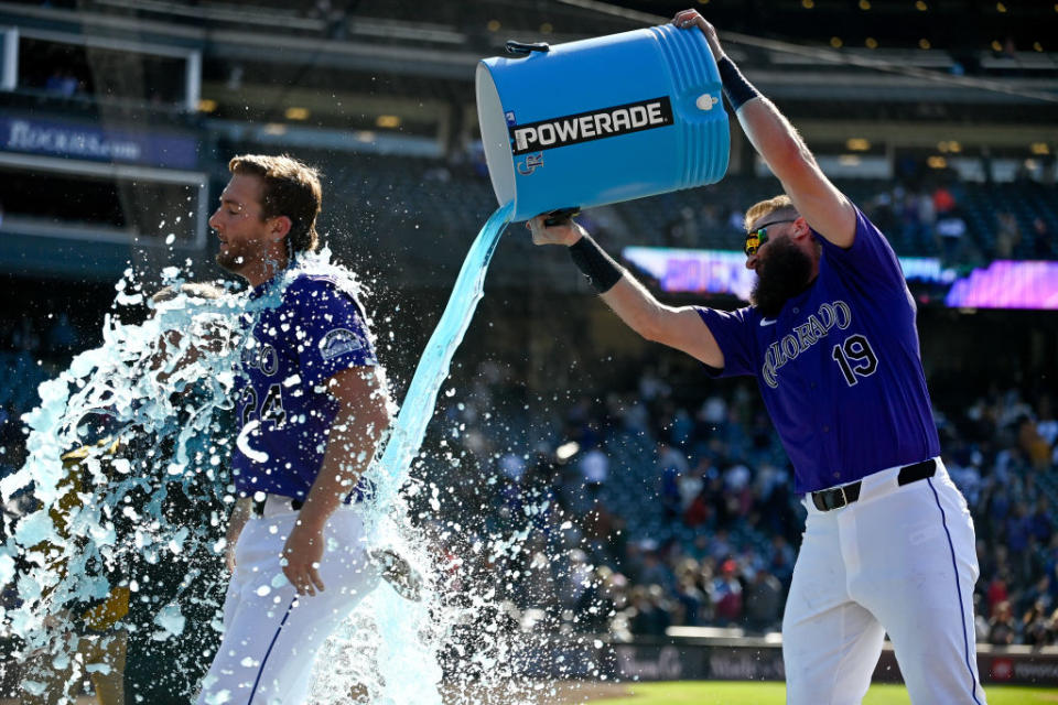 A baseball player, wearing jersey number 19, pours a large cooler of blue Powerade over a teammate's head, celebrating on the field in front of cheering fans