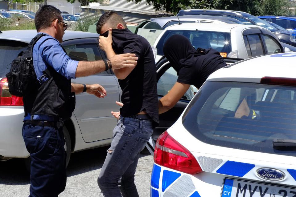 Two suspects cover their faces with their shirts as they arrive at the Famagusta courthouse in Paralamni town, Cyprus, Thursday, July 18, 2019. A Cyprus court has ordered 12 Israelis vacationing on the east Mediterranean island nation to remain in police custody for eight days after a 19-year-old British woman alleged that she was raped. (AP Photo/Petros Karadjias)